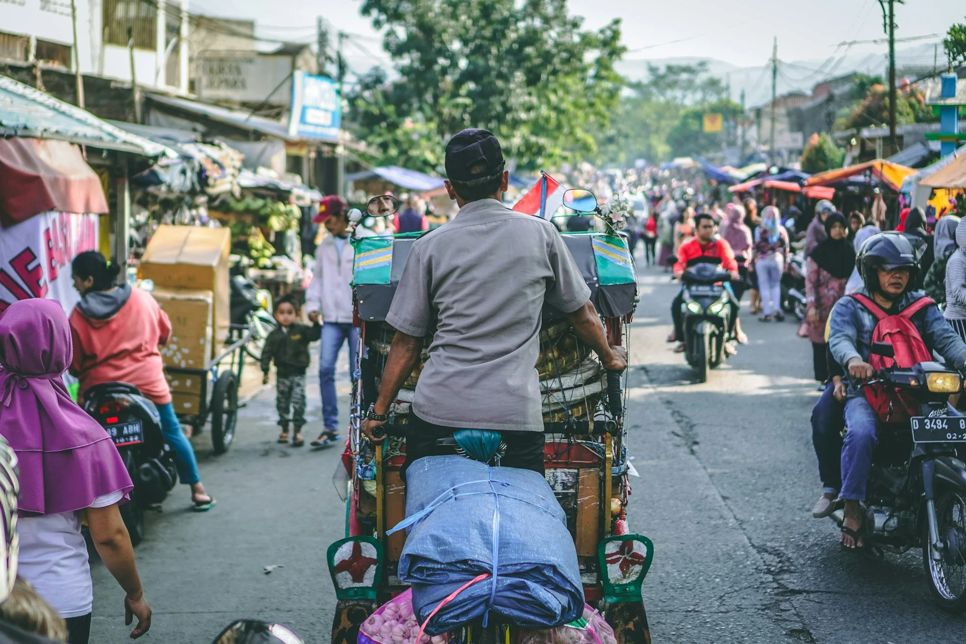 Seorang pedagang mengayuh kendaraan dagang di jalan