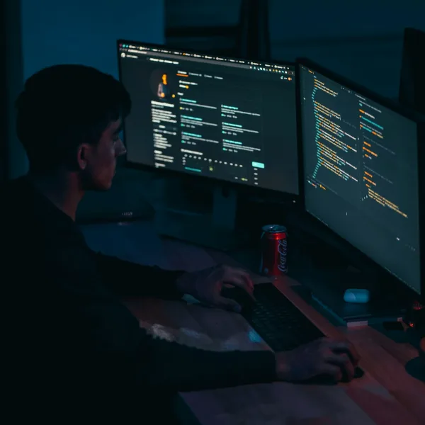 Seorang pengembang berbaju hitam bekerja di depan monitor komputer
