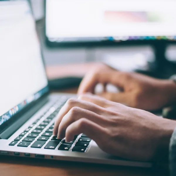 Seseorang mengetik pada laptop di atas meja kayu